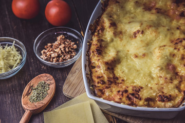 lasagne layered served on a wooden board with fresh tomatoes alongside
