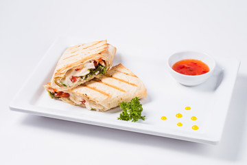 Traditional mexican tortila wrap with meat and vegetables on a white plate on a light background.
