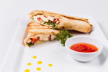Traditional mexican tortila wrap with meat and vegetables on a white plate on a light background.