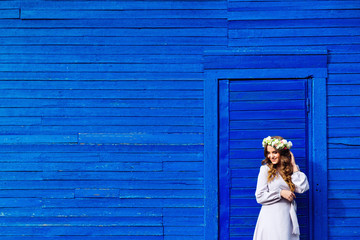 the girl stands at the door in the blue house and fixes a wreath of flowers that is in her head
