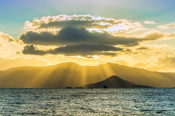 Ein von Sonnenstrahlen durchflutete Wolke über dem Meer mit Bergen im Hintergrund, goldene Stunde
