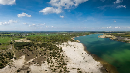 Ein See mit einem angrenzenden Dorf im Frühling als Luftbild von oben. Entstanden ist das Aerial mit einer Drohne