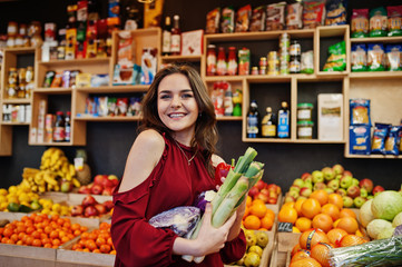 Girl in red holding different vegetables on fruits store.