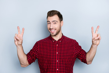 Fototapeta premium Portrait of careless cheerful relaxed free and easy guy clothed in red checkered shirt demonstrating two fingers, isolated on gray background