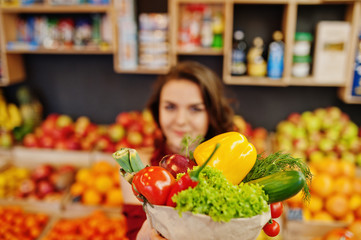 Girl in red holding different vegetables on fruits store.