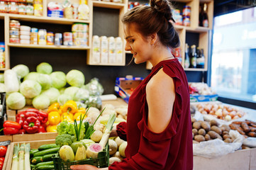 Girl in red holding different vegetables on fruits store.