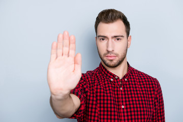 Stop and ponder! Close up portrait of serious confident frowning attractive wearing red casual checkered shirt hipster demonstrating stop sign with his hand, isolated on gray background, copy-space