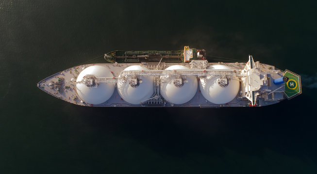 A top view of a small tanker on a roadstead unloads a large LNG tanker.