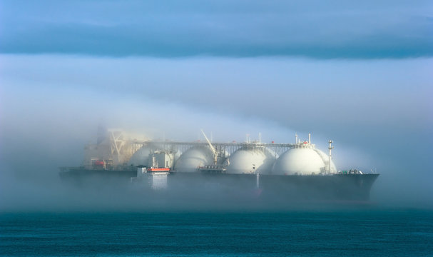 A small tanker on the roads unloads a large LNG tanker in the fog.