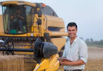 Engineer with notebook and combine harvester in field