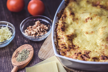 lasagne layered served on a wooden board with fresh tomatoes alongside