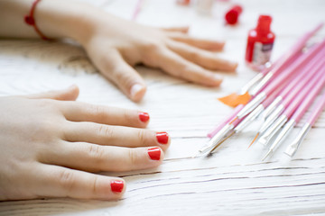 Obraz na płótnie Canvas mom paints daughter's nails on hands with red nail Polish on white table, beautiful nails concept, manicure
