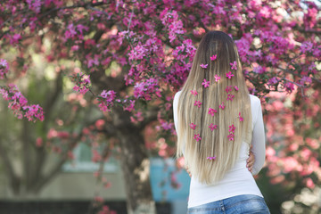 Young girl standing her back to the camera on the floral background with flowers in her hair