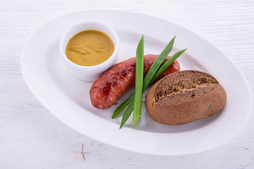 Mustard sauce, black bread, pork sausage on a white plate with green onions