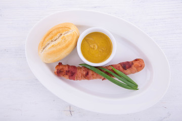 The sausage fried with bacon is served on a white plate and on a white wooden background