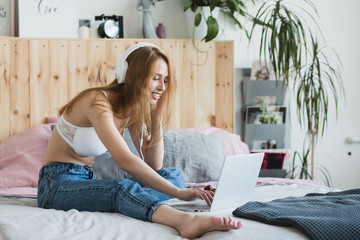 Obraz premium Young sexy blonde woman flirting online on laptop, sitting on bed in bedroom