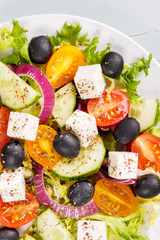 Greek salad with feta cheese, olive, tomatoes, cucumbers, peppers and oil olives in white plate. Restaurant menu. Free space for text. White background.