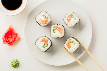 Roll of sushi on a plate, Sushi roll on a tablet on the table restaurant / eating sushi roll using chopsticks, white background, Sushi roll and hand with chopsticks. Japanese food.
