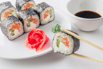 Roll of sushi on a plate, Sushi roll on a tablet on the table restaurant / eating sushi roll using chopsticks, white background, Sushi roll and hand with chopsticks. Japanese food.