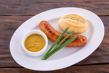 Sausage from chicken with white loaf and mustard sauce, with feathers of green onions on a black wooden background