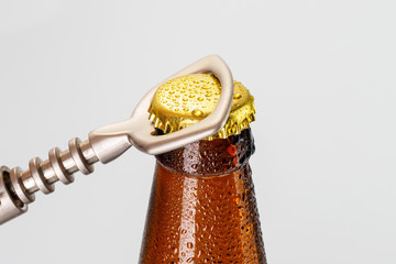 A hand opening a fresh cold ale bottle of beer with drops and stopper open with bottle opener on white background.