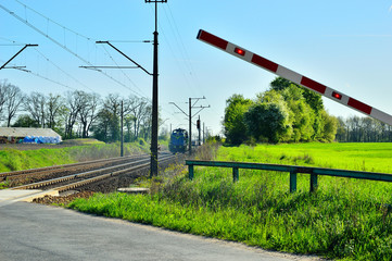 Szlaban kolejowy w ruchu i przejazd kolejowy z jadącą lokomotywą.