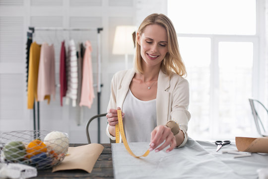 Scrupulous work. Inspired female dressmaker working with fabric and holding meter