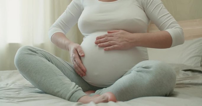 a pregnant girl with a big belly strokes her belly, communicating with the baby in the womb, close-up