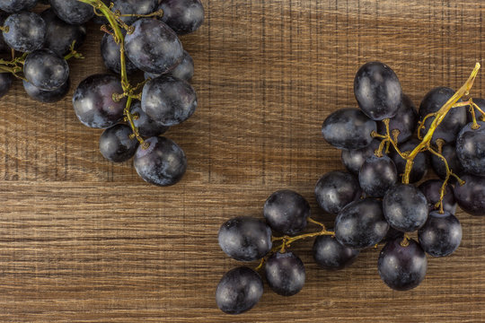 Black grape two clusters (autumn royal variety) table top isolated on brown wood background.