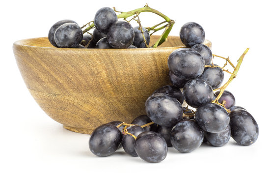 Black grape cluster (autumn royal variety) in a wooden bowl isolated on white background.
