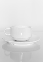 White coffee cup on a white plate on a white background.