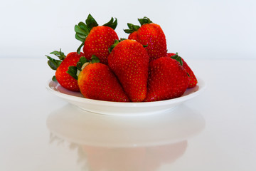 A large red strawberry lies on a white plate.