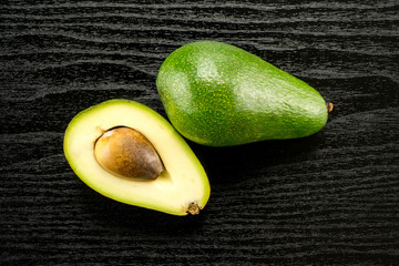 Green smooth avocado and one section half with a seed table top isolated on black wood background...