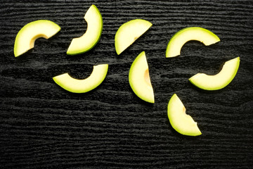 Green smooth avocado halved slices top view isolated on black wood background bacon variety.