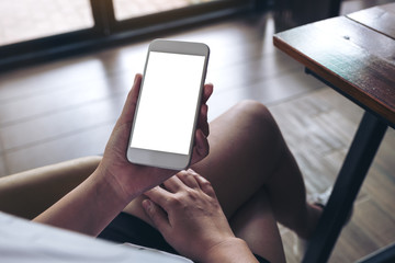 Mockup image of woman's hands holding white mobile phone with blank desktop screen sitting in cafe