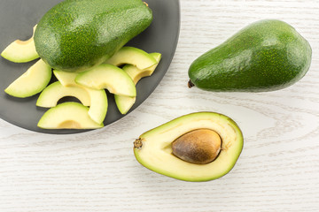 Green smooth avocado sliced composition on a grey plate table top isolated on light wood background...