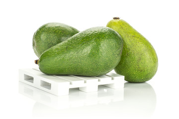 Three green smooth avocado on a wooden pallet isolated on white background ripe shiny bacon variety.