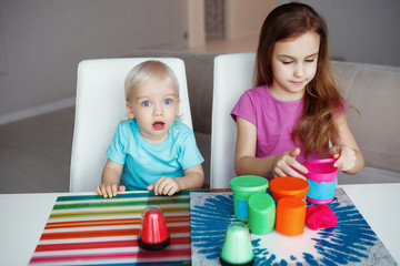 Two happy children Blond boy and girl playing sitting at table at home