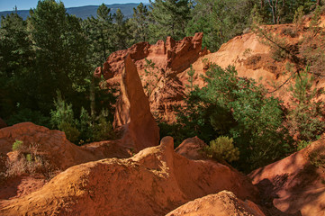 View of ocher land, trees under a sunny blue sky, in the park "Sentiers des Ocres", near the village of Roussillon. Located in the Vaucluse department, Provence region, in southeastern France