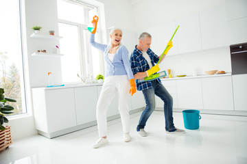 Full size, fullbody portrait of crazy foolish funny mad cool couple of senior dancing, singing, man playing on mop like guitar, woman holding spray in raised hand, positive people concept