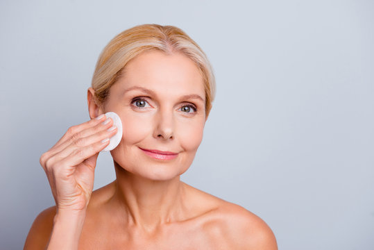 Portrait of pretty charming stylish attractive woman with wrinkle applying lotion using cotton pad cleaning make-up looking at camera isolated on grey background