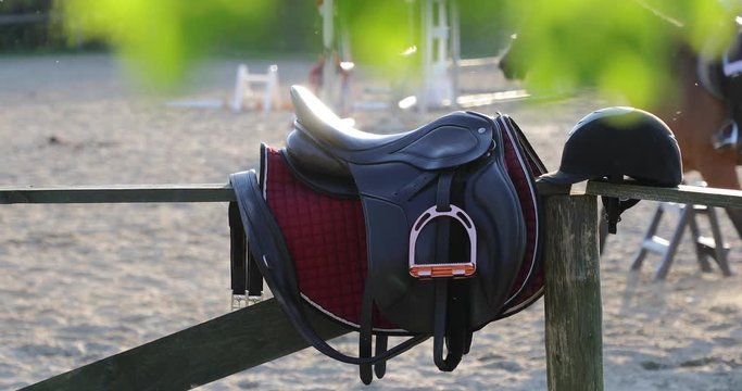 Horseback saddle on the wooden fence on the background of training riders in a sunny day