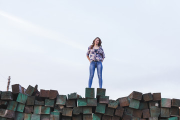 Obraz premium portrait of a young beautiful woman wearing casual clothes, standing on a mountain of green wood blocks background and smiling. Outdoors lifestyle.