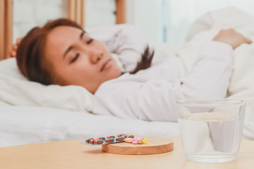 Fototapeta na wymiar Closeup on pills and glass of water on table and Asian women sleep sick on bed in bed room