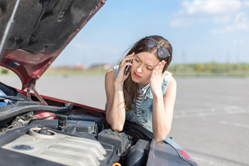 Girl near a broken car on the country road is calling on mobile phone.
