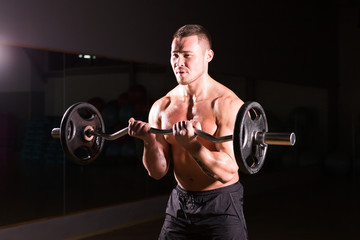Naklejka na ściany i meble Muscular young man lifting weights on dark background