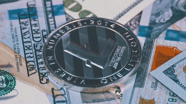 Silver Litecoin Coin, LTC and Bills of Dollars are Rotating. Crypto Currency Close-up. Macro. Dollar banknotes of various denominations on which lies the cryptocurrency.