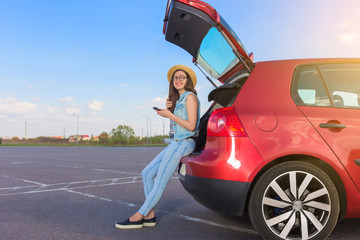 Young woman traveler sitting on hatchback car with outdoor sunny  background 
