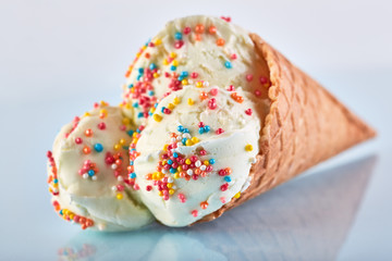 ice cream balls with colored sugar sprinkles in a Waffle Cone on a Blue Background. Vanilla ice cream in a waffle cone.