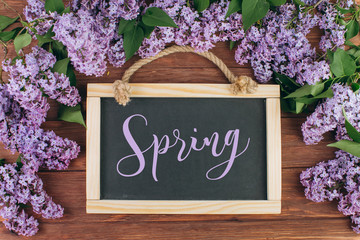 Chalkboard with description "Spring" on a wooden background with lilac.